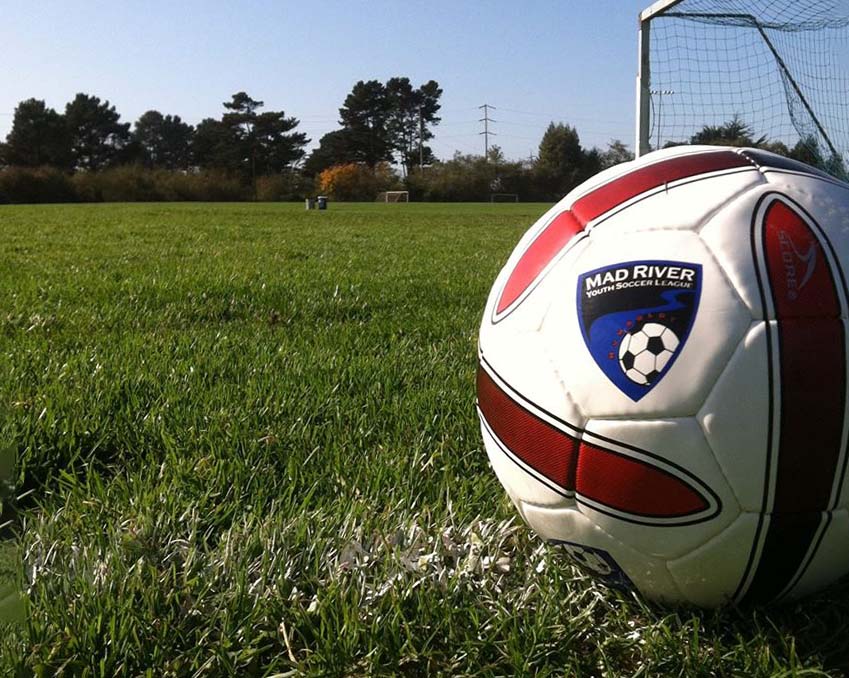 A soccer ball with the MRYSL logo sits on the grass in front of a goal net